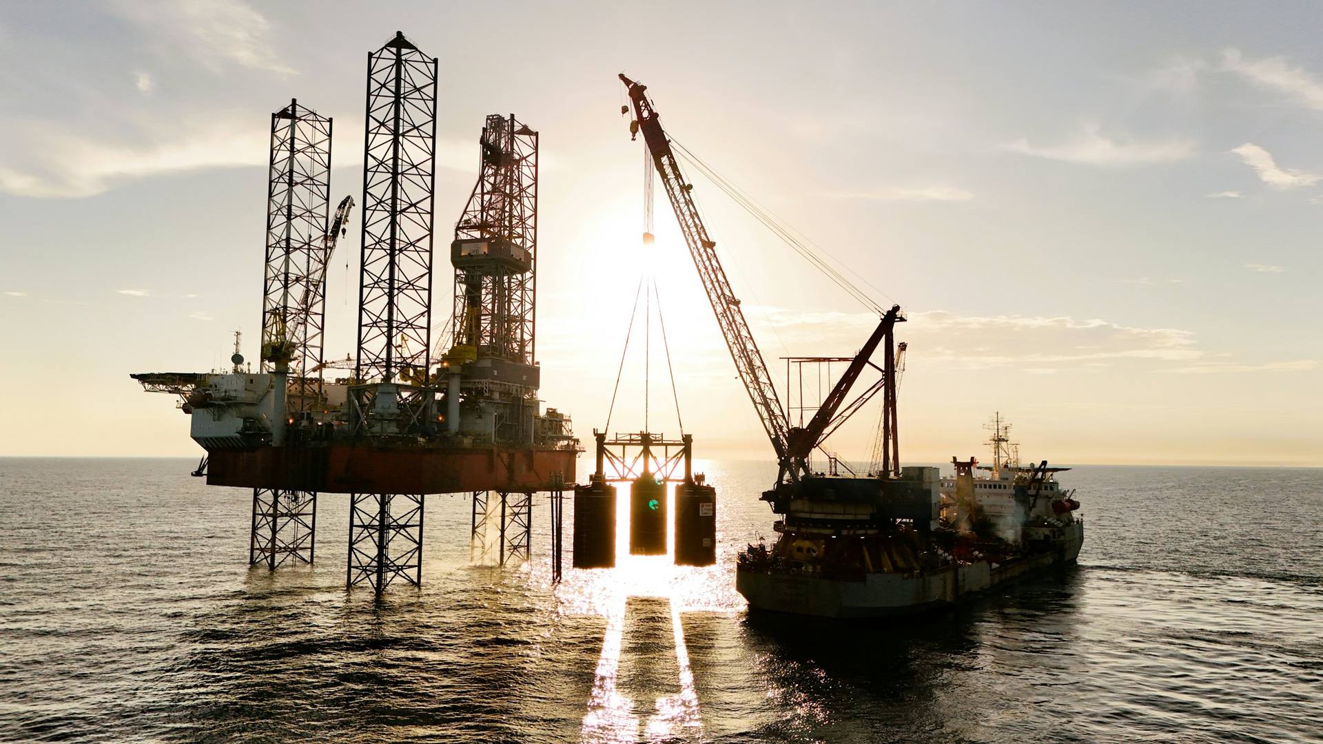 Offshore jack-up drilling unit with a support vessel at sunset